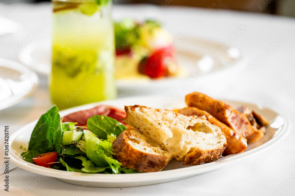 A close-up of a breakfast plate featuring fresh salad, slices of crusty bread, and meats. A refreshing mint drink in the background complements the colorful meal. A close-up of a breakfast plate featuring fresh salad, slices of crusty bread, and meats. A refreshing mint drink in the background complements the colorful meal.