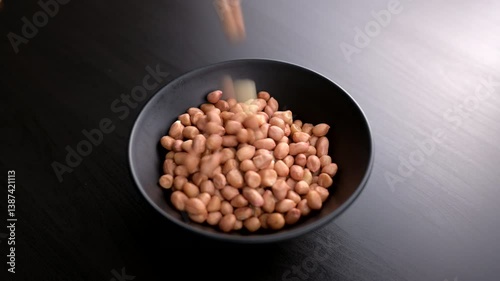 Raw Peanuts Falling into a Black Bowl on Wooden Table. Minimalist Food Footage Perfect for Healthy Eating, Organic Snacks, or Cooking Prep Scenes