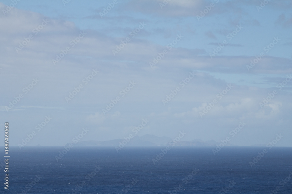 Fototapeta premium Misty ocean view with a distant island barely visible through the thick fog. Calm and moody atmosphere with soft, diffused light over the water.