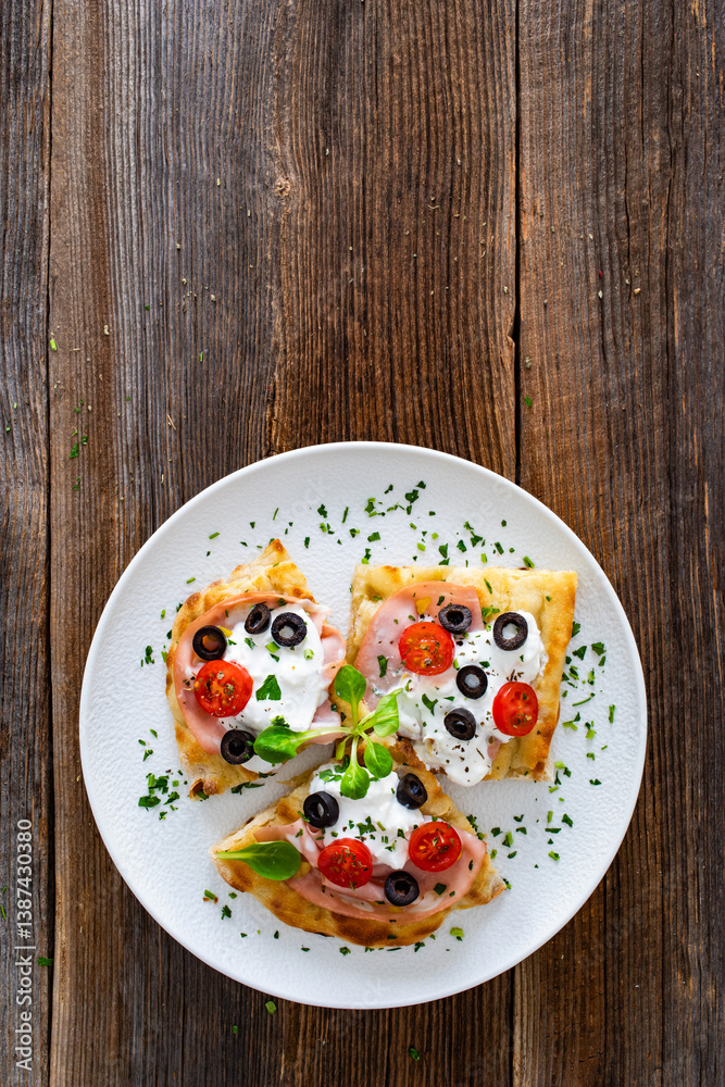 Pinsa Romana with mortadella, burrata cheese, black olives and cherry tomatoes on wooden table Pinsa Romana with mortadella, burrata cheese, black olives and cherry tomatoes on wooden table
