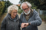 An elderly man and an elderly woman checking vitals in a smartwatch during a walk outside in nature