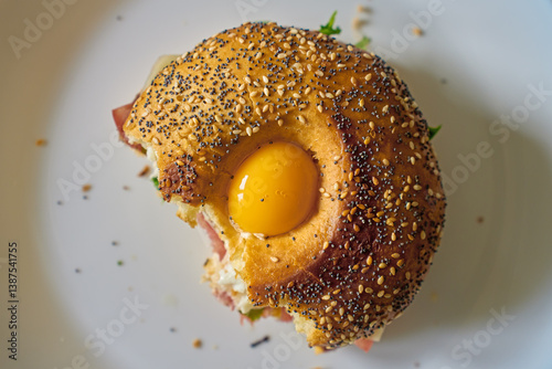 Obraz na płótnie Close-up of bitten bagel with egg, ham, cheese and fresh greens. Half-eaten breakfast sandwich on plate, top view w salonie