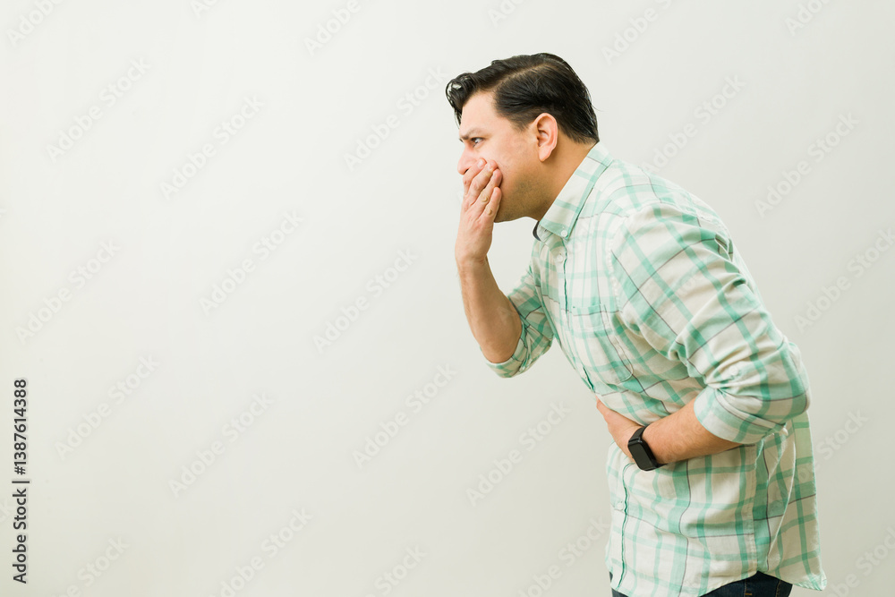 Male experiencing nausea, pressing hand against mouth while clutching stomach in discomfort Male experiencing nausea, pressing hand against mouth while clutching stomach in discomfort