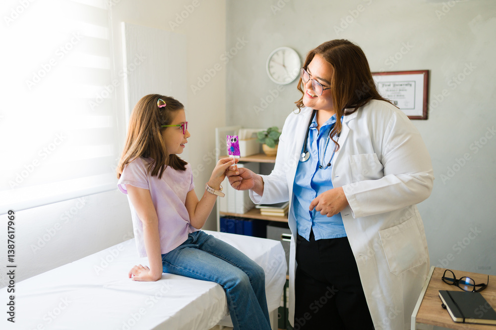 Kind female pediatrician giving a lollipop to a little girl patient after a successful checkup in the doctor's office