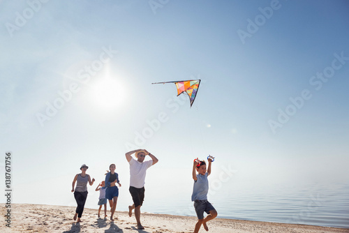 A happy family is relaxing during the summer holidays. Children, their parents fly a kite on the riverbank