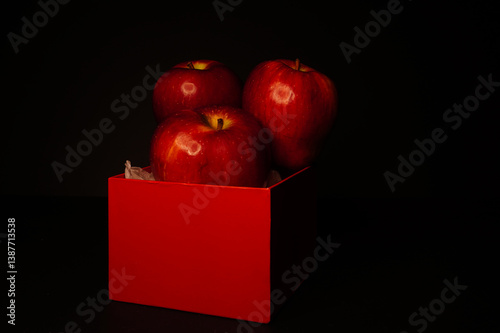 Red apples and red boxes on a black background, with dim lighting to simulate a chiaroscuro effect