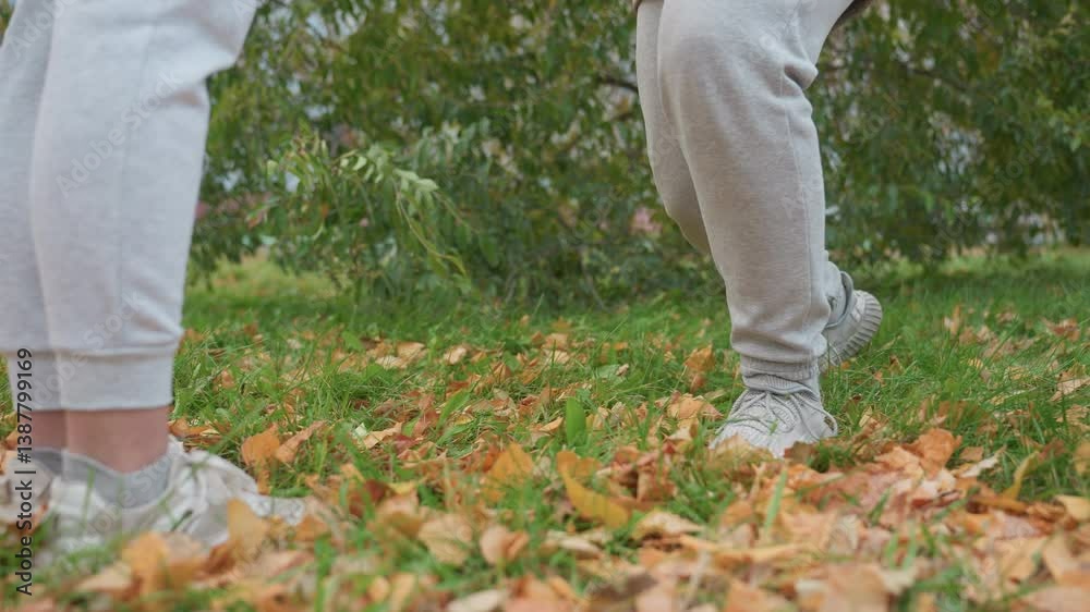 Lower body view of people in matching outfits as one gets on knees surrounded by green grass, dry autumn leaves, and distant view of building during emotional outdoor moment Lower body view of people in matching outfits as one gets on knees surrounded by green grass, dry autumn leaves, and distant view of building during emotional outdoor moment