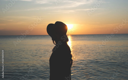Silhouette rear view of a woman with hat looking at a beautiful sunset and the sea view