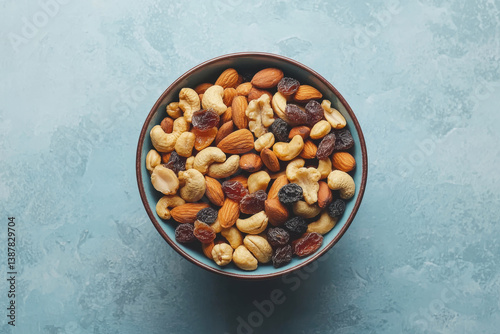 Obraz na płótnie Top view of ceramic bowl filled with assorted nuts and dried fruits. Mixed almonds, cashews and raisins nuts on blue background. Healthy snack concept w salonie