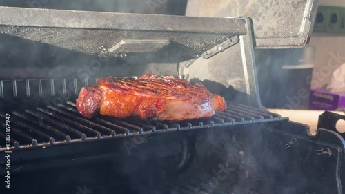 Close-up steak grilling on BBQ grid. Roasting tomahawk steak on barbecue grill. Grilling BBQ meat. Smoke rising over beef steak