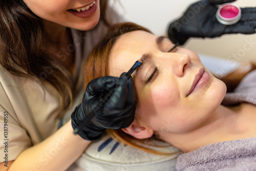 Photography Beauty professional applying eyebrow tint to a woman's brows using a fine brush
