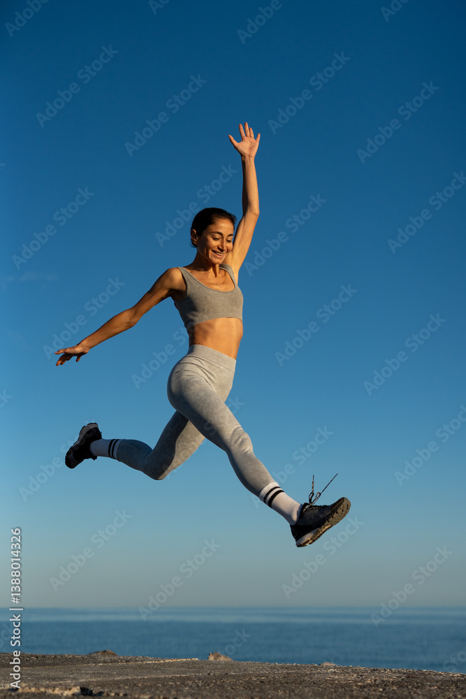 Strong and graceful: woman mid-air during a fitness leap by the sea Strong and graceful: woman mid-air during a fitness leap by the sea