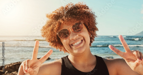  Woman, curly hair and sunglasses , smiling, peace and backdrop of ocean waves and rocky coastline under a clear sky. High quality photo
