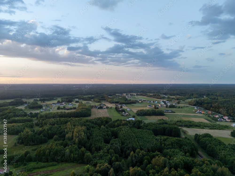 Aerial view of a serene rural landscape at sunset, showcasing lush greenery, fields, and residential homes against a picturesque sky with dynamic clouds. Aerial view of a serene rural landscape at sunset, showcasing lush greenery, fields, and residential homes against a picturesque sky with dynamic clouds.