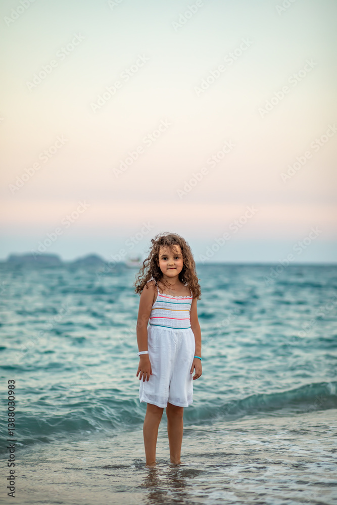 Cute little girl standing on the seashore at the beach near by sea or ocean in summer. Playful active kid. Holiday vacation with children. Cute little girl standing on the seashore at the beach near by sea or ocean in summer. Playful active kid. Holiday vacation with children.
