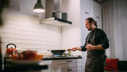 A male cook is cooking at the stove at home in the kitchen