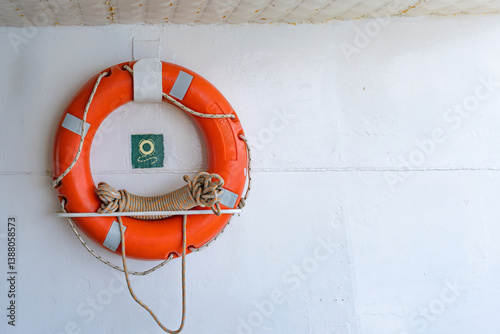 Orange Life Preserver On Ship Wall. Lifebuoy with Rope Hanging on a White Wall. Maritime Safety And Emergency Preparedness Concept