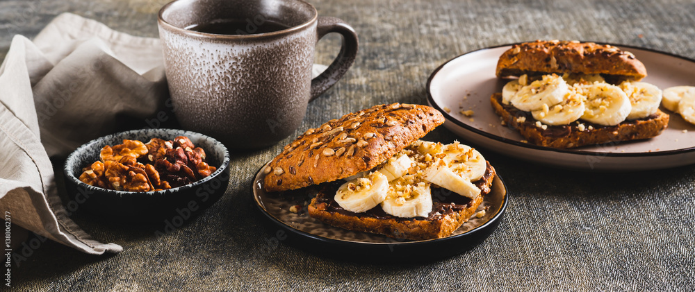 Sweet sandwich with chocolate butter, banana and nuts on a plate on the table web banner