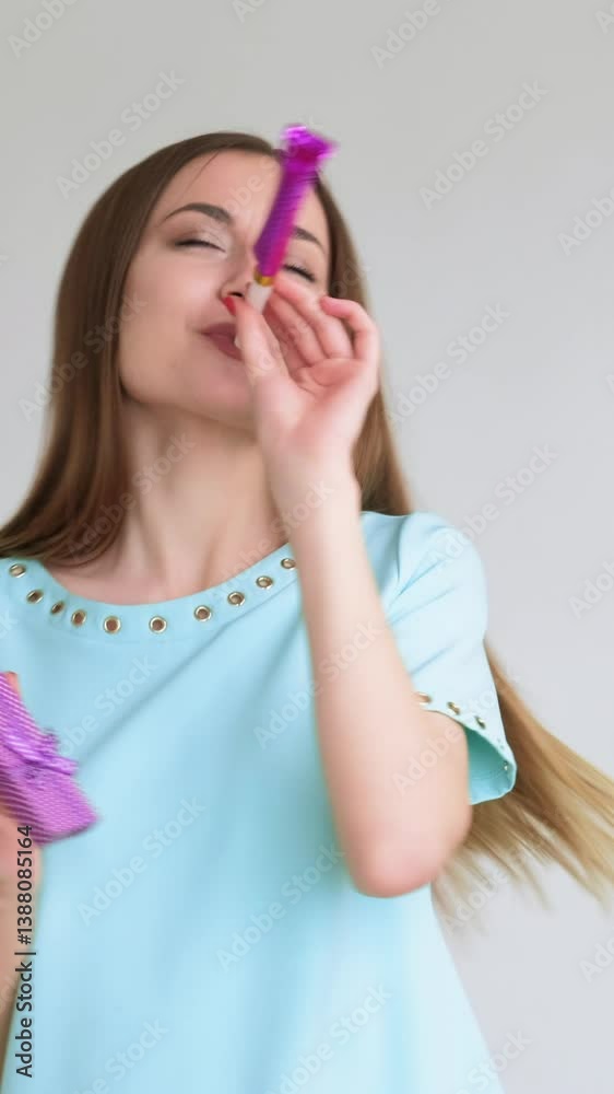 Vertical video. Party emotion. Special day. Portrait of happy amused woman in blue dancing alone with jewelry box smiling blowing horn isolated on light. Vertical video. Party emotion. Special day. Portrait of happy amused woman in blue dancing alone with jewelry box smiling blowing horn isolated on light.