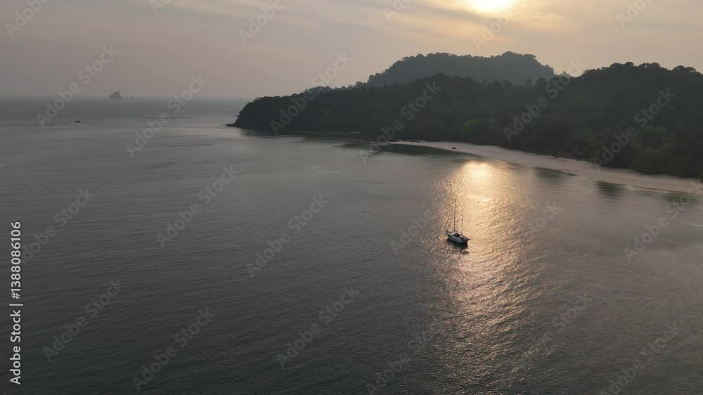 Aerial sunset view of yacht anchored in clear sea waters near the coastline of a tropical island in the Andaman Sea, Thailand Aerial sunset view of yacht anchored in clear sea waters near the coastline of a tropical island in the Andaman Sea, Thailand