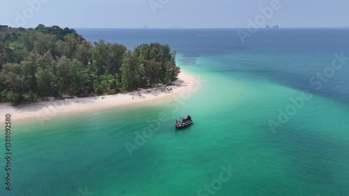 Aerial view of Thai traditional longtail fishing boat floating in transparent turquoise sea waters with reef near shoreline of tropical island in Andaman sea, Thailand