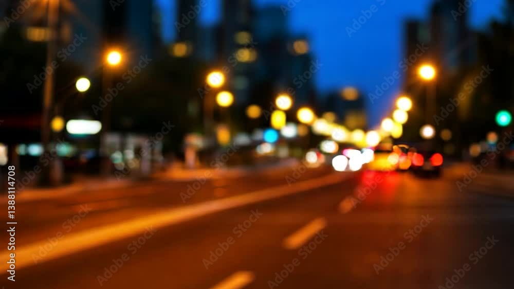 Blurred city street at night with illuminated buildings and moving vehicles in the background Blurred city street at night with illuminated buildings and moving vehicles in the background