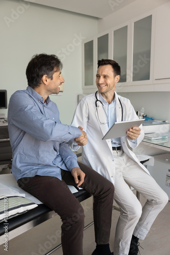 Satisfied middle-aged patient received clear explanation of condition agreed on treatment plan, shake hands smiling professional therapist or cardiologist dressed in white uniform. Successful recovery