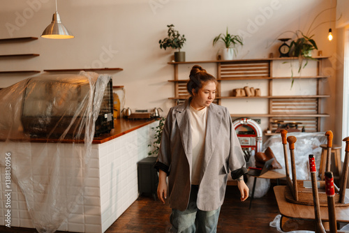 Female owner walks and looks at chairs on tables, preparing for cafe opening