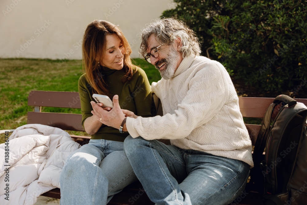 A man sits on a bench and looks while holding his hand near the phone held by a woman sitting next to him, they are laughing, on the street, on a date A man sits on a bench and looks while holding his hand near the phone held by a woman sitting next to him, they are laughing, on the street, on a date