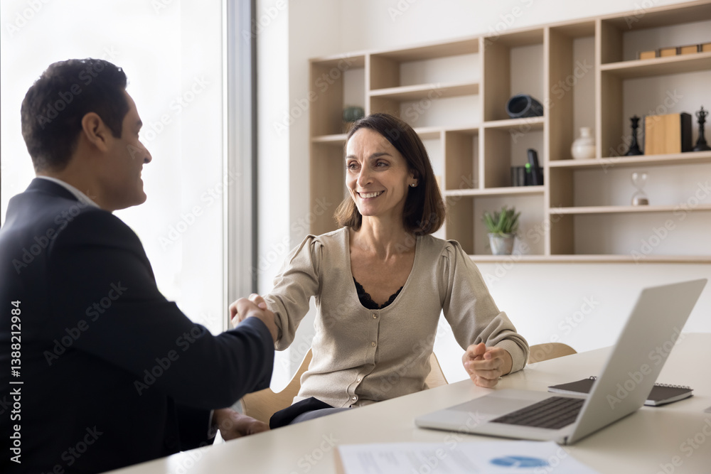 Obraz premium Latin and Indian business parties finish negotiations shaking hands seated at desk in meeting room, gesture of successful agreement, conclude professional partnership, making deal. Sell, buy services