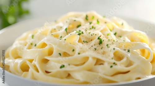 Creamy fettuccine alfredo fills a white bowl. The pasta is coated in a rich, white sauce and sprinkled with parmesan cheese and parsley. The image is high-quality, well-lit, and shows a close-up vie