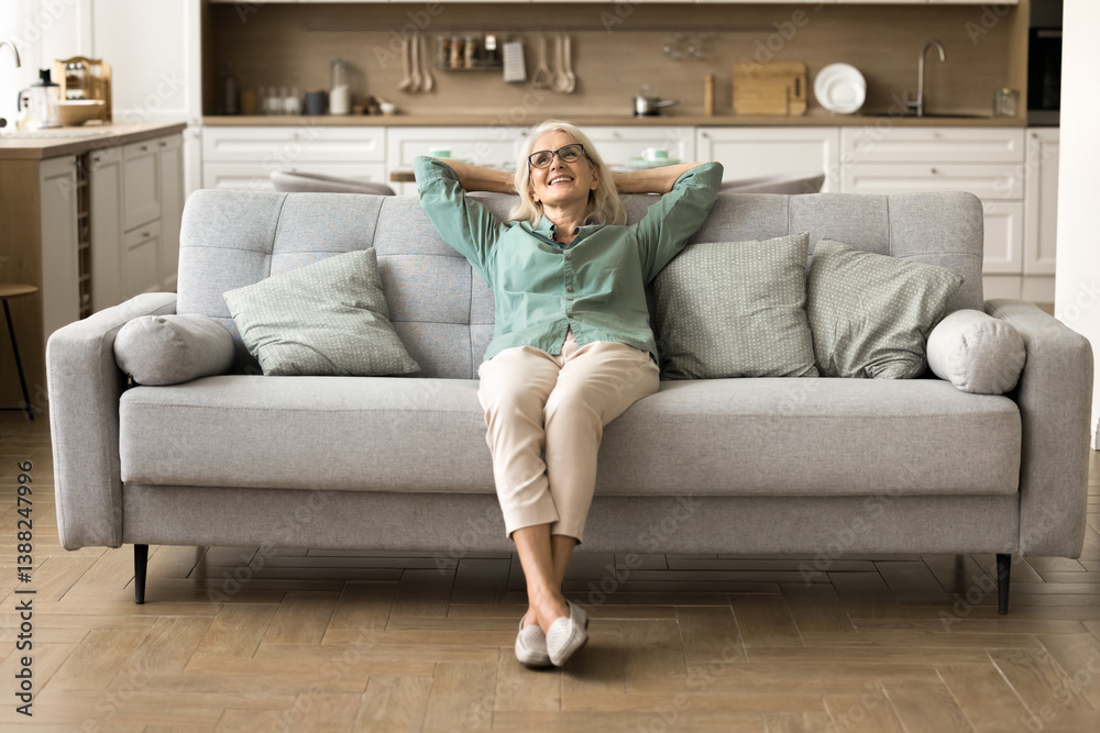 Finding peace at cozy home. Serene tranquil older woman homeowner renter tenant enjoy moment of relax on comfy sofa listen to music feel peace of mind in clean light interior of large studio apartment Finding peace at cozy home. Serene tranquil older woman homeowner renter tenant enjoy moment of relax on comfy sofa listen to music feel peace of mind in clean light interior of large studio apartment