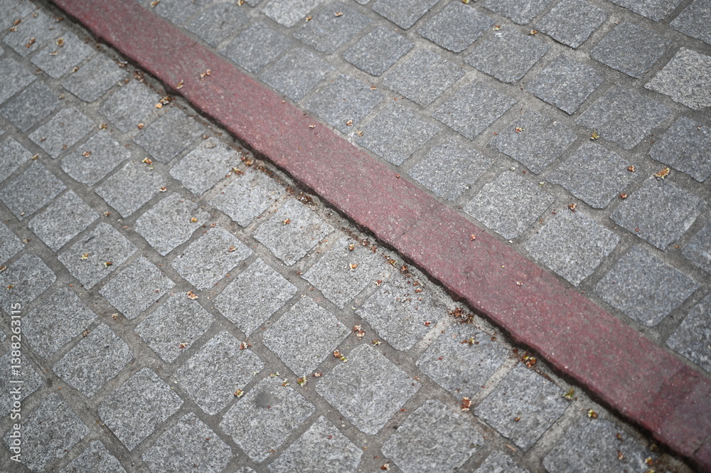 Fototapeta premium Stone pavement with red line marking. Urban cobblestone texture background, old European street detail.