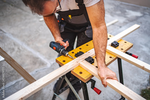 Mature male carpenter using electric screwdriver on a wooden plank outdoors