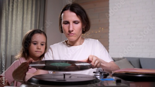 Woman and a little girl are carefully putting a vinyl record on a turntable, ready to enjoy listening to music together