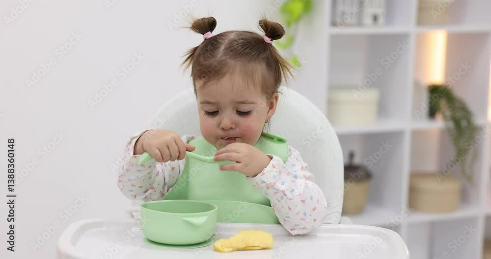 Cute little baby eating healthy food and showing thumbs up in high chair indoors Cute little baby eating healthy food and showing thumbs up in high chair indoors
