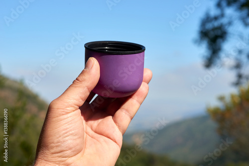 Mountain valley backdrop highlighting hands gripping purple insulated tumbler with steaming beverage, capturing peaceful outdoor relaxation moment