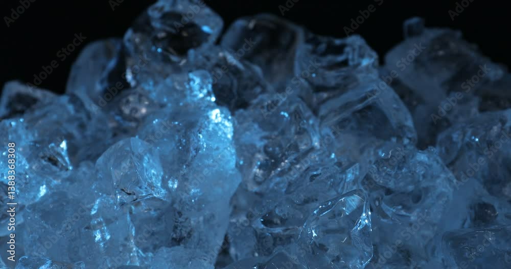 Many crystal clear ice cubes in blue light on black background, closeup. Camera moving up