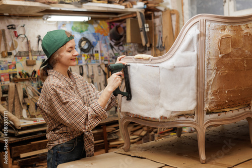 Female upholsterer using staple gun while restoring a vintage chair in a cozy workshop.