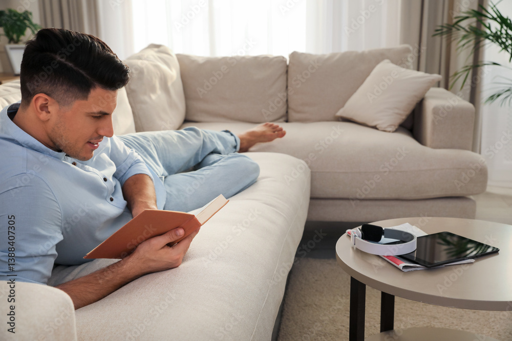 Man reading book on sofa in living room Man reading book on sofa in living room