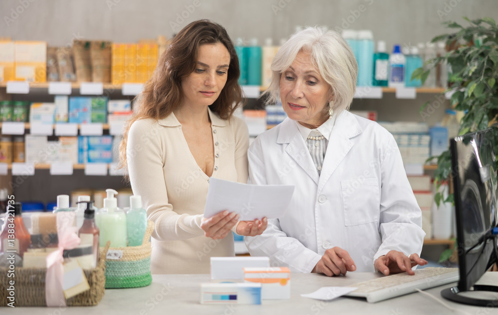 Mature woman pharmacist at computer communicate with female client. Employee answers visitors questions, interprets doctors prescription, selects available drugs for treatment regimen