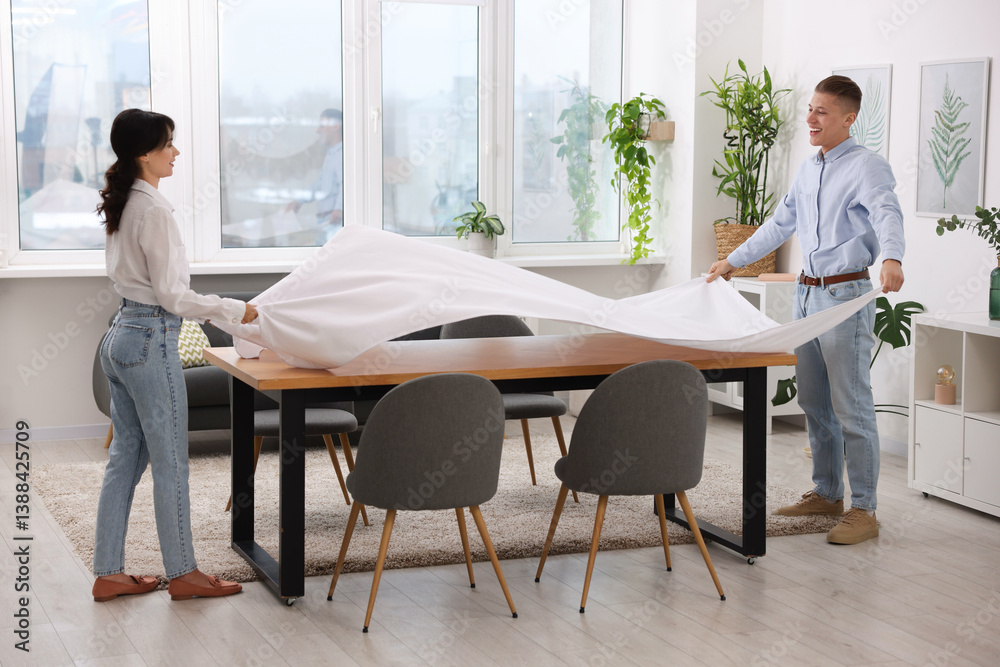 Couple putting white tablecloth on table at home Couple putting white tablecloth on table at home