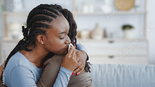Slika na platnu Crying young black woman hugging her girlfriend or sister, living room interior, copy space