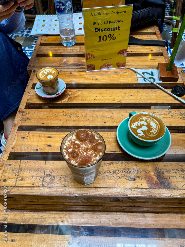 Magic Coffee with two ristretto shots and steamed milk served in a turquoise cup, held over a wooden table with pastries and drinks, capturing a cozy café moment.
