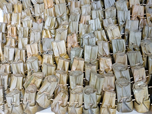 The background of this lontong display is filled with neatly arranged cylindrical rice cakes wrapped in banana leaves. The leaves have dried to a muted green-brown shade, tied with small bamboo sticks