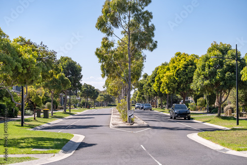 A suburban intersection with a straight asphalt road framed by mature trees and manicured lawns on the median and nature strip.A clean, well-defined street in a neighborhood.Williams Landing,Australia