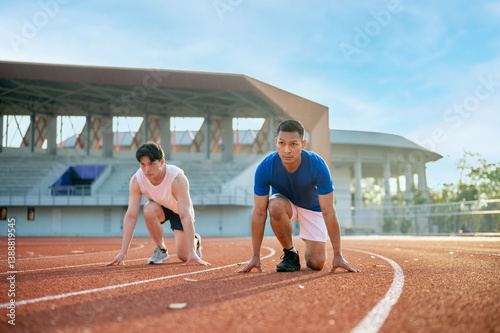 Картината върху платно Two asian athlete men in a crouch start or starting position ready to run on the racetrack