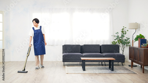 部屋の床に掃除機をかけるエプロンをつけたミドル女性