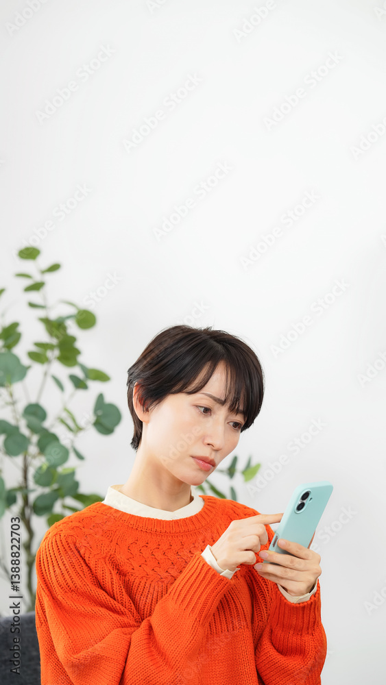 リビングルームで悩みながらスマホを見るミドル女性 リビングルームで悩みながらスマホを見るミドル女性