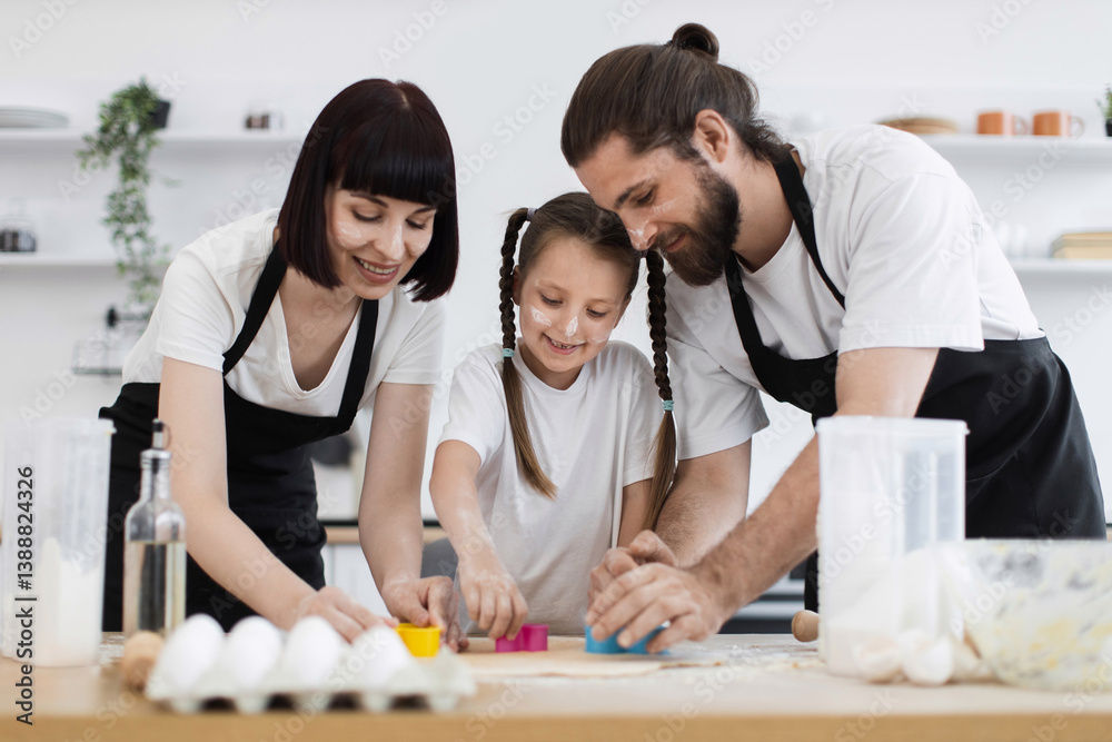 Obraz premium Caucasian family, including a young daughter, joyfully baking cookies together in a modern kitchen. They use molds to cut dough and share a fun, bonding experience full of smiles and creativity.